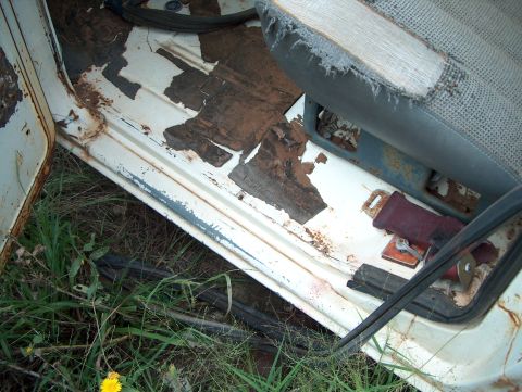 1979 Ford Bronco - The interior of an old vehicle shows significant rust and wear on the floor and seat.