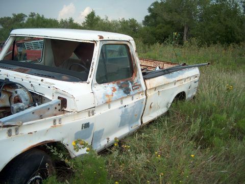 1979 Ford Bronco - A weathered white pickup truck sits in a field, showing signs of disrepair and age.