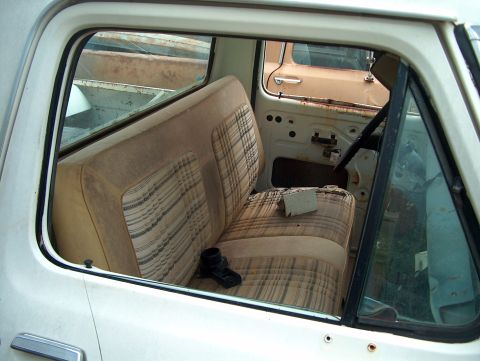 1979 Ford Bronco - Interior of a white pickup truck with a bench seat and removed door panel, another vehicle is visible outside.
