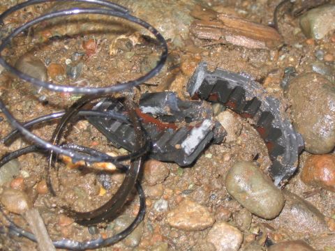 1989 Ford Bronco - A damaged automotive belt lies on the ground, its internal structure exposed amidst rocks and mud.