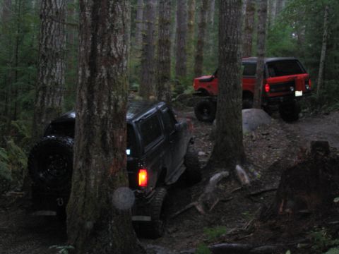 1989 Ford Bronco - A black 1989 Ford Bronco navigates a wooded trail, with a red SUV following behind.