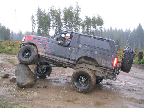 1989 Ford Bronco - Driver navigates a challenging off-road obstacle in a modified 1989 Ford Bronco.
