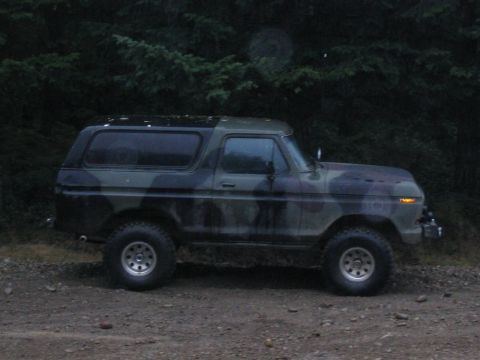 1989 Ford Bronco - This 1989 Ford Bronco, seen in a side profile, is painted in a camouflage pattern and parked on a gravelly surface with trees in the backgr…