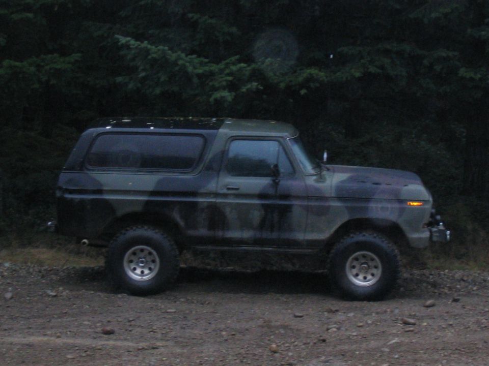 Side view of a camouflaged 1989 Ford Bronco parked on a dirt road