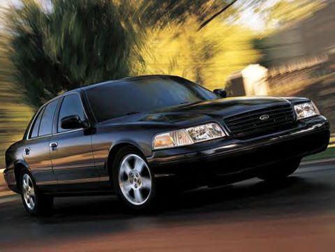 1999 Ford Crown Victoria - Three-quarter front view of a black Ford Crown Victoria full-size sedan driving on a road, shot with a panning motion blur that streaks the…