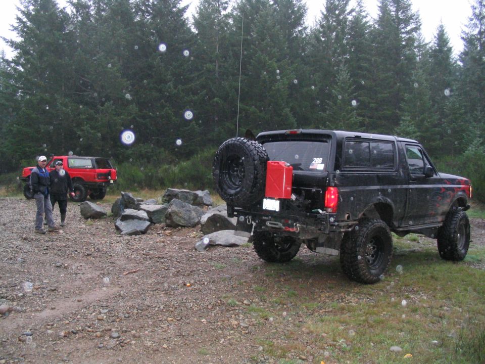 Black Ford Bronco with spare tire and gas can on back, red Bronco in background