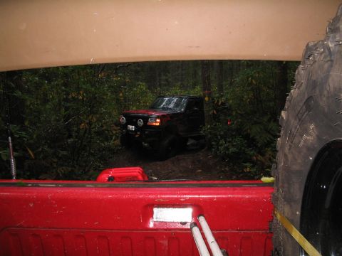 1989 Ford Bronco - A black 1989 Ford Bronco navigates a muddy off-road trail surrounded by dense forest.
