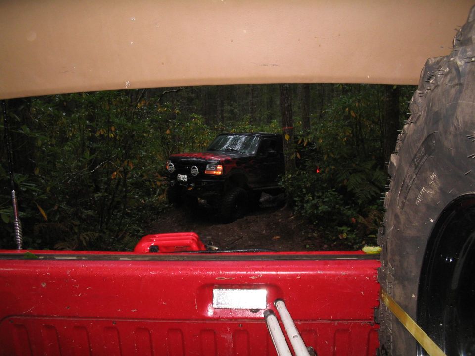 Black 1989 Ford Bronco on a muddy trail, viewed from the rear of another vehicle