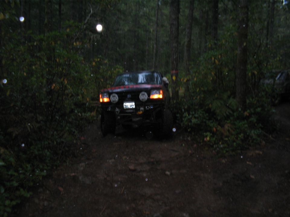 1989 Ford Bronco driving on a muddy forest trail, front view