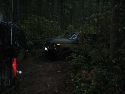 1989 Ford Bronco - Two off-road vehicles navigate a dense forest trail in low light conditions.