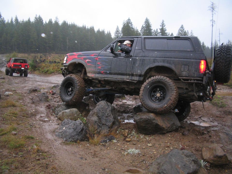 Black 1989 Ford Bronco on rocks, side view. Flame decals on hood and doors