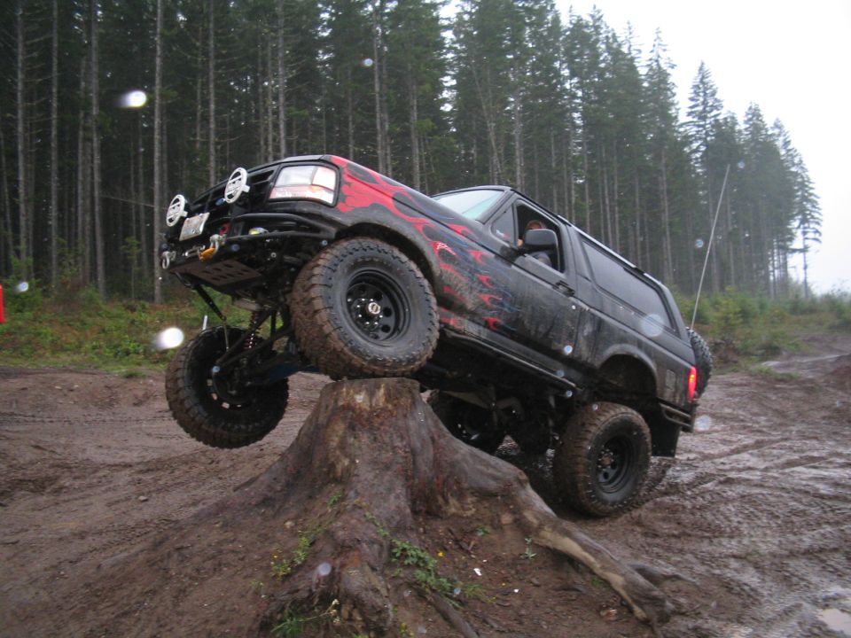 Black Ford Bronco with red flame decals on a large tree stump, front passenger wheel elevated