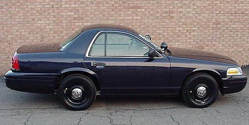 Digitally shortened two-door Ford Crown Victoria police car in dark blue, side view against a brick wall