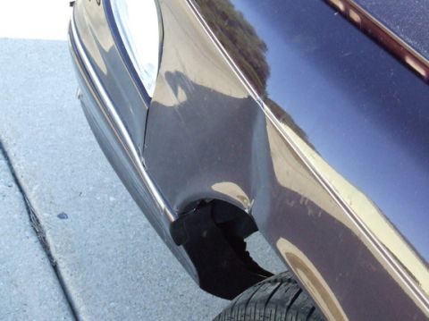 1992 Ford Crown Victoria - The rear fender of a car shows significant damage, with a tire visible below.
