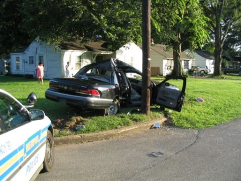 1999 Ford Crown Victoria - A severely damaged black sedan is pictured after colliding with a utility pole, with a police vehicle in the foreground.