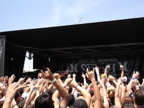 1992 Ford F-150 - A large crowd cheers with hands in the air at an outdoor concert, with a band performing on stage in the background.