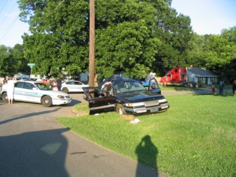 1999 Ford Crown Victoria - A black sedan is heavily damaged after crashing onto a grassy area, with its doors ajar.