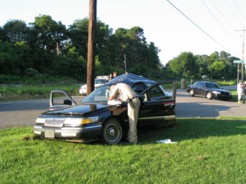 1999 Ford Crown Victoria - A 1999 Ford Crown Victoria is examined by a person in uniform after an apparent incident, with another vehicle visible in the background.