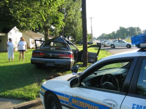 1999 Ford Crown Victoria - A damaged sedan is attended to by police after an apparent accident, with onlookers present.