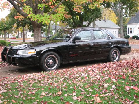 2000 Ford Crown Victoria - A black sedan with a push bumper is parked on a street covered in fallen leaves.