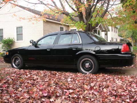 2000 Ford Crown Victoria - A black 2000 Ford Crown Victoria sedan is parked on a street covered in fallen autumn leaves.