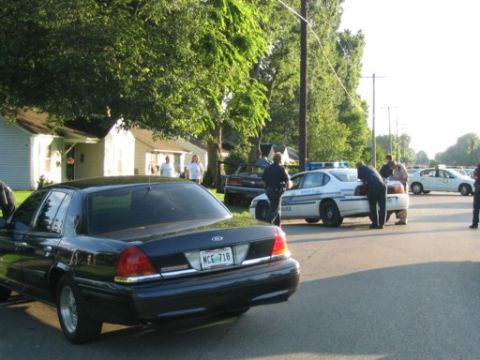 1999 Ford Crown Victoria - A black 1999 Ford Crown Victoria is seen from the rear, parked on a street with other vehicles and people present.