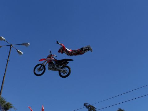 1989 Ford Bronco - A motorcycle stunt rider is captured in mid-air alongside their dirt bike against a bright blue sky.