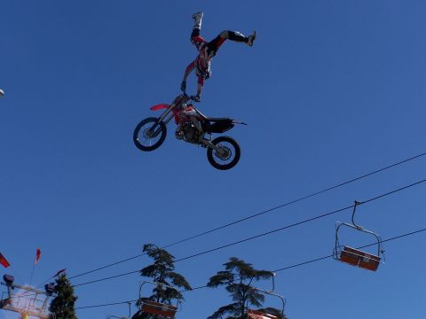 1989 Ford Bronco - A motocross rider performs a daring stunt while airborne on a dirt bike, with ski lift chairs visible below.