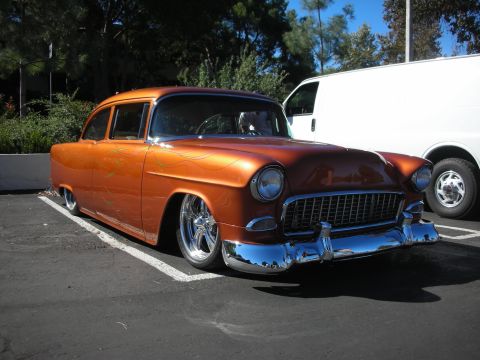 1998 Ford Crown Victoria - copper-orange custom 1955 Chevrolet two-door sedan, lowered on chrome wheels, parked at a car show.