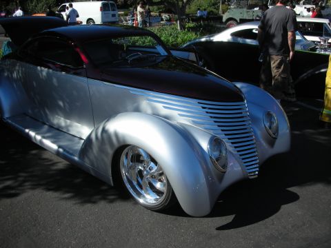 1998 Ford Crown Victoria - silver streamlined custom coupe with a black top and louvered hood sides on polished wheels at an outdoor show.