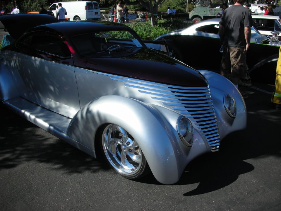 Silver custom streamlined coupe with black top and louvered hood, polished wheels at a car show