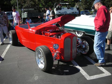 1998 Ford Crown Victoria - red highboy roadster hot rod with its hood open sits among spectators at an outdoor car show.