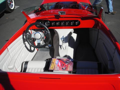 1998 Ford Crown Victoria - red-and-white custom interior of an open roadster with a row of gauges, a small steering wheel and a car magazine on the seat.
