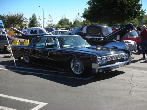 1998 Ford Crown Victoria - black lowered 1960s Lincoln Continental four-door with wire wheels parked among other cars at an outdoor show.