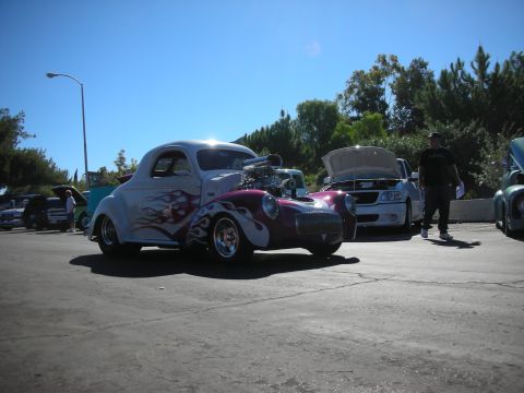 1998 Ford Crown Victoria - white hot rod coupe with purple flames and an exposed supercharged engine parked among other cars at an outdoor show.