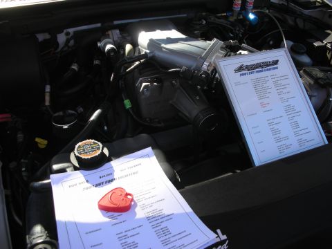 1998 Ford Crown Victoria - Engine bay of a supercharged truck with display spec sheets titled 2001 SVT Ford Lightning resting on the engine.