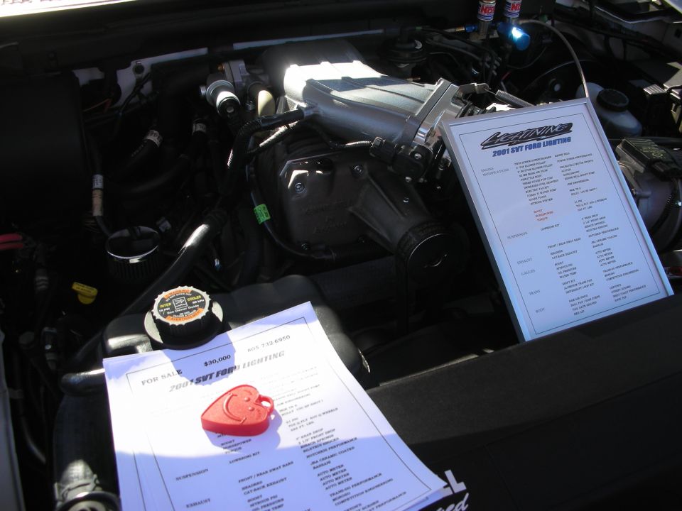 Modern truck engine bay with supercharger and printed spec sheets for a 2001 SVT Ford Lightning