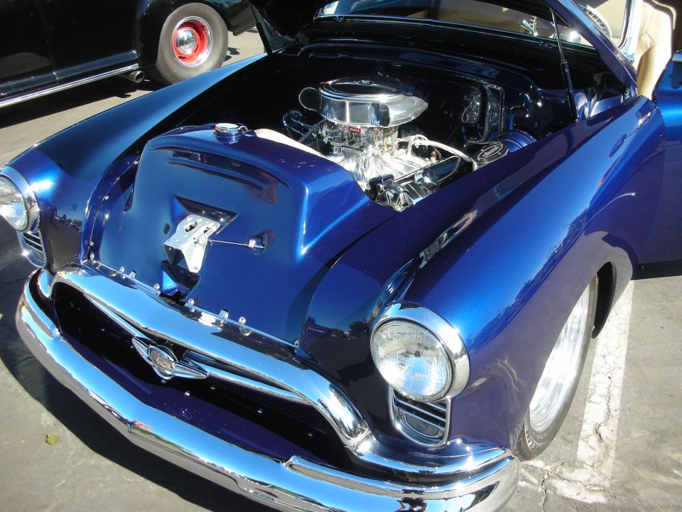 Blue 1950s-era custom coupe with open hood revealing a chrome V8 engine