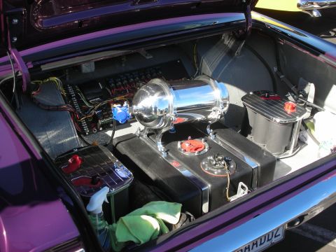 1998 Ford Crown Victoria - Open trunk of a purple custom car showing a polished air tank, fuel cell, battery box and exposed wiring on black carpet.