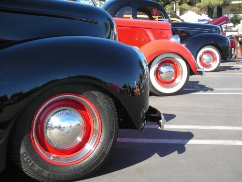 1998 Ford Crown Victoria - Rear three-quarter view of a row of vintage hot rod coupes lined up, with red-painted steel wheels and wide tires.