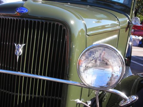 1998 Ford Crown Victoria - Close-up of a green vintage Ford's front end showing the blue Ford oval, a V8 grille badge and a chrome headlight.