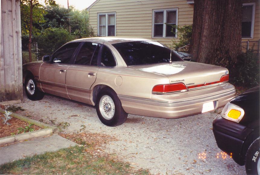 Gold Ford Crown Victoria rear three-quarter parked on gravel in a backyard setting