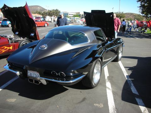 1998 Ford Crown Victoria - black Chevrolet Corvette Sting Ray coupe shown rear-three-quarter with its hood up at a sunny outdoor car show, plate reading TALL'S 63.
