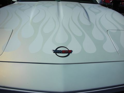 1998 Ford Crown Victoria - Close-up of a white car hood decorated with subtle ghost-flame graphics and a round crossed-flags emblem at center.