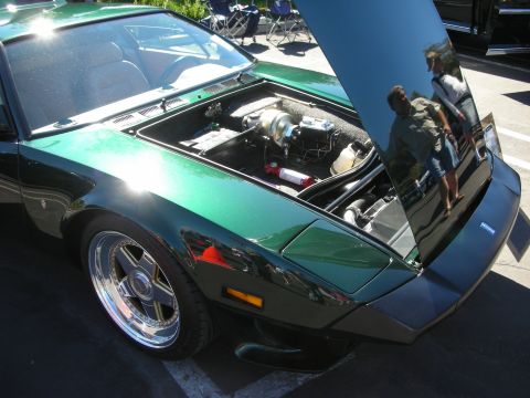 1998 Ford Crown Victoria - metallic green wedge-shaped sports car with its rear engine hatch raised, polished five-spoke wheels, and spectators reflected in the glass.