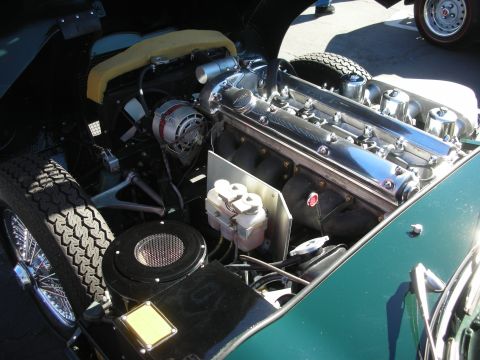 1998 Ford Crown Victoria - Jaguar inline-six engine showing twin polished camshaft covers and SU intakes, with a spare wire wheel and tire visible alongside.