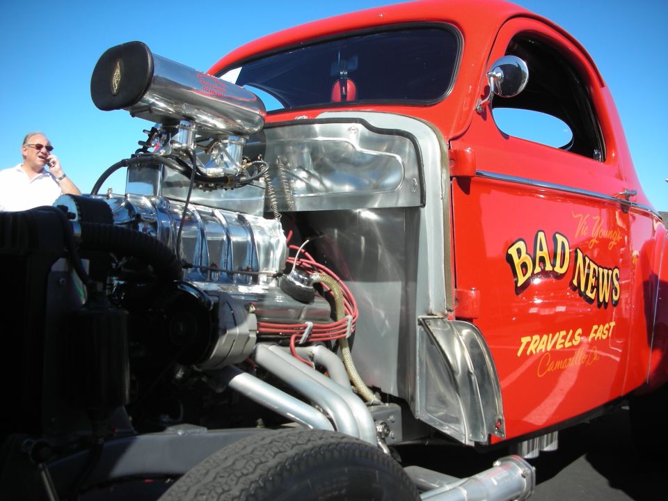 Red pickup hot rod with exposed supercharged engine lettered Bad News Travels Fast