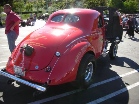 1998 Ford Crown Victoria - Rear three-quarter view of a red gasser-style coupe with sponsor lettering on the body, tall rear tires, and a raised front end.