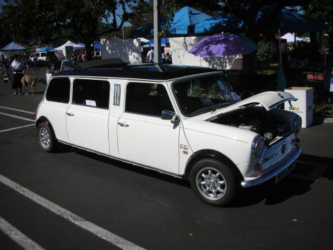 1998 Ford Crown Victoria - white classic Mini stretched into a multi-door limousine, hood open, parked on asphalt at an outdoor show.