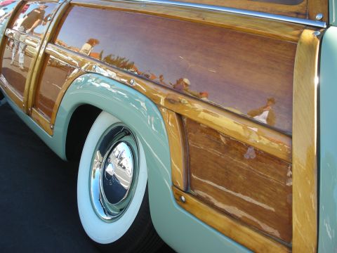 1998 Ford Crown Victoria - Detail shot of glossy wood side paneling and a chrome-hubcap whitewall wheel on a restored woodie wagon.